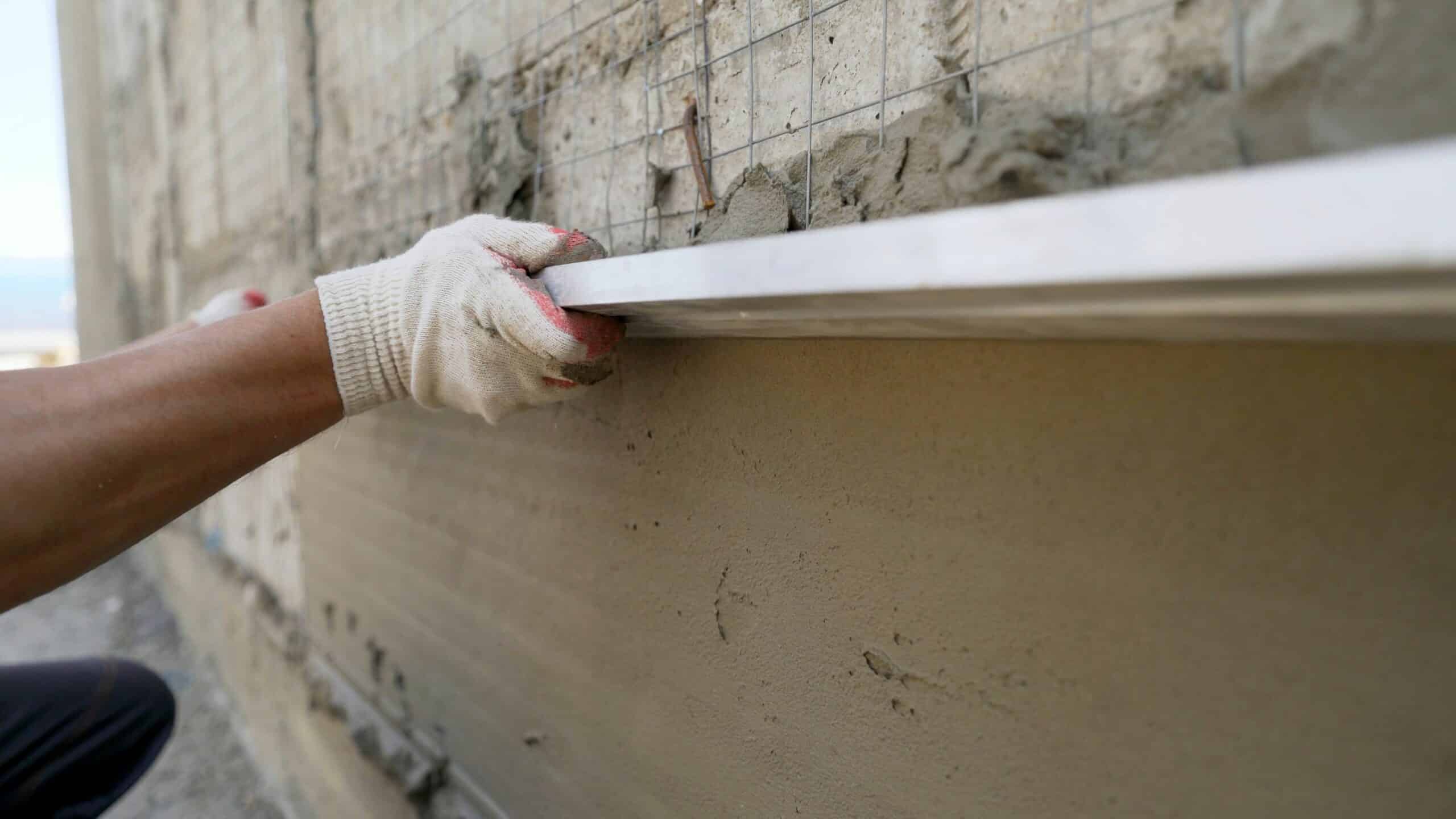 Applying and leveling the wall using construction tools. Leveling the mortar on the wall using a rule. A male builder uses a rule to plaster a wall outdoors.